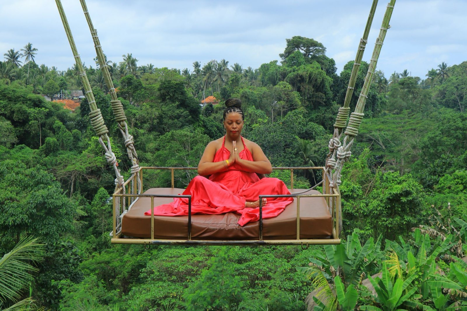 Qiana meditating on a swing bed above a jungle canopy